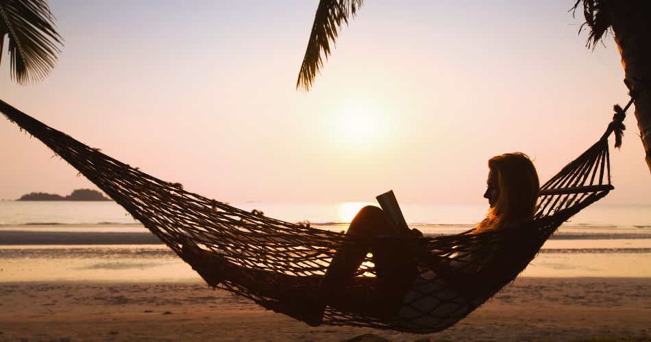 Relaxed woman lying on a hammock with a book against a sunset backdrop in Goa, enjoying the susegad lifestyle.